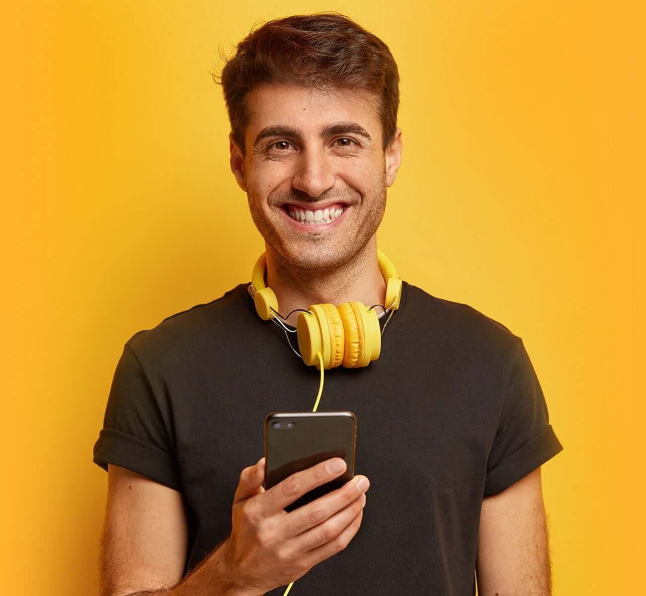 man-phone-orange-background » HCi Smiling young man holding a phone and wearing orange head phones, all on an orange background » HCi